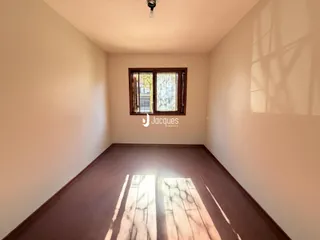 Ambiente interno de uma sala com piso de madeira escura e janela.