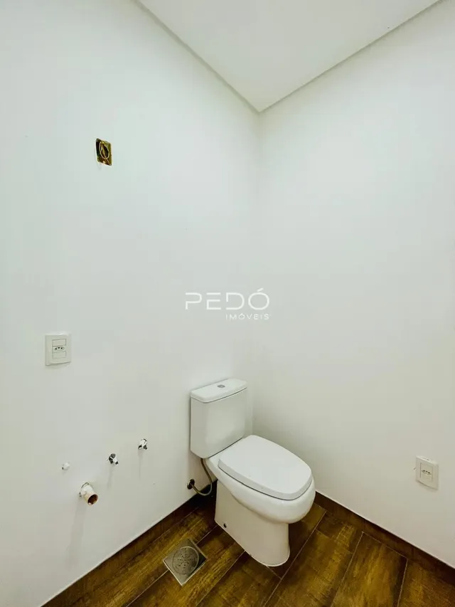 Foto interna de um banheiro com piso de madeira e paredes brancas.