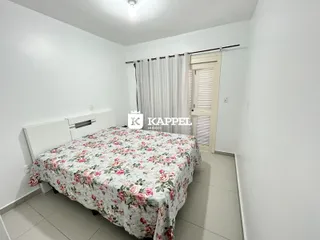 Quarto com cama de casal coberta por lençol floral e cortinas brancas.