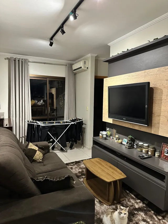 Sala de estar com sofá e televisão montada na parede em um imóvel.