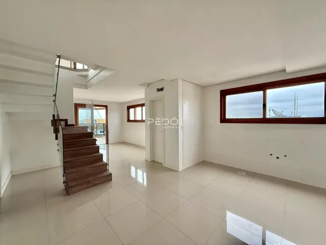 Ambiente interno de uma sala ampla com piso claro e escadaria de madeira.