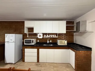 Cozinha com armários brancos e bancada escura em ambiente de tijolos aparentes.