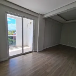 Vista interna de uma sala com piso de madeira e porta de vidro que dá para o exterior.