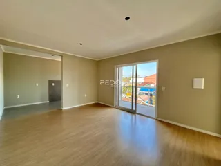 Sala de estar ampla com piso de madeira clara e porta de vidro.