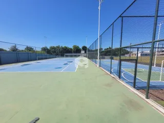 Uma quadra esportiva externa com piso azul cercada por uma cerca de arame.