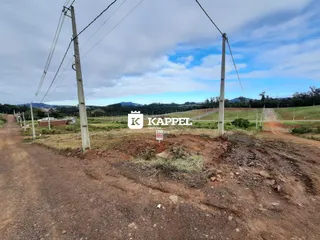 Vista de uma estrada de terra em uma área rural com vegetação e colinas ao fundo.