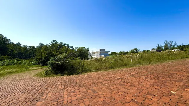 Vista externa de uma propriedade com paisagem verde e pavimento de tijolos.