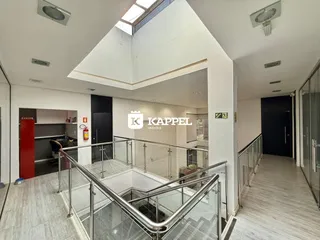 Vista de um corredor com escadaria e guarda-corpo de vidro em um imóvel.