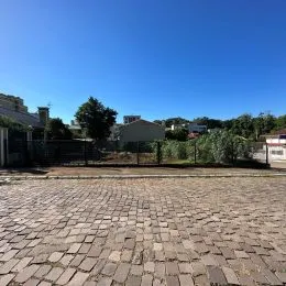 Vista externa da propriedade com piso de paralelepípedos sob céu azul.