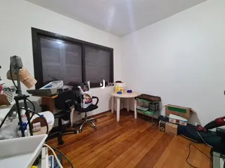 Ambiente interno de uma sala com piso de madeira e janela com venezianas.
