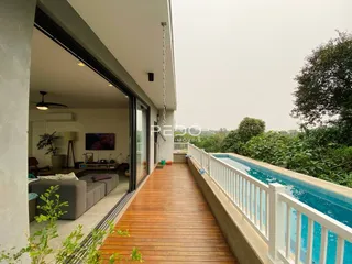 Sala de estar com vista para uma piscina e jardim através de uma passarela de madeira.