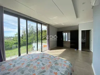 Quarto com vista para a paisagem verde através de grandes janelas.