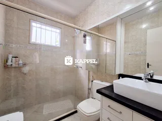 Banheiro com revestimento de azulejos claros e box de vidro transparente.