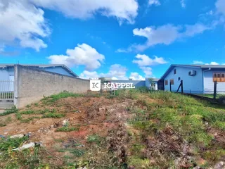 Vista externa da propriedade mostrando um terreno com vegetação rasteira e uma residência ao fundo.