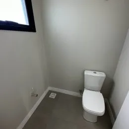 Corredor interno com parede branca e vaso sanitário visível.