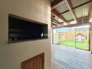 Parede interna com televisão montada e acesso a uma área externa com deck de madeira.