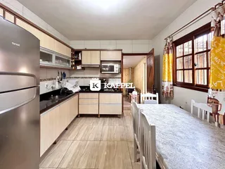 Cozinha com armários de madeira clara e bancadas escuras, com mesa de jantar em primeiro plano.