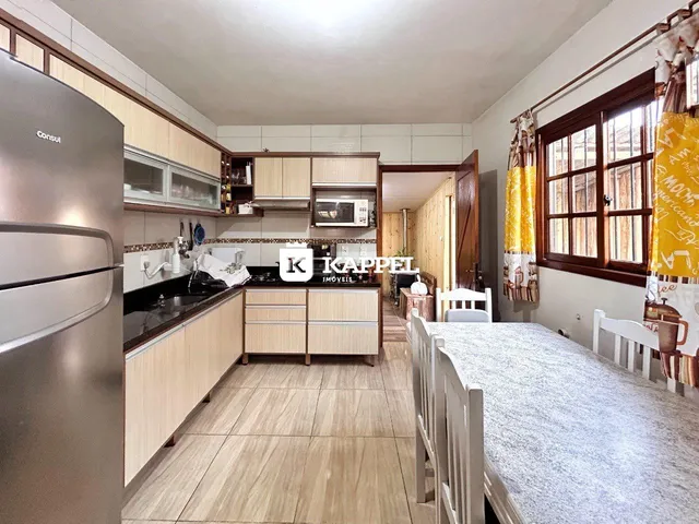 Cozinha com armários de madeira clara e bancadas escuras, com mesa de jantar em primeiro plano.
