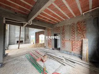 Uma vista interna de uma estrutura em construção com vigas expostas e materiais de construção no chão.