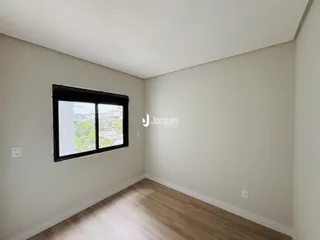 Quarto interno com janela e piso de madeira clara.