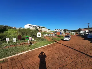 Vista externa de uma estrada de terra com vegetação e edifícios ao fundo em Lajeado.