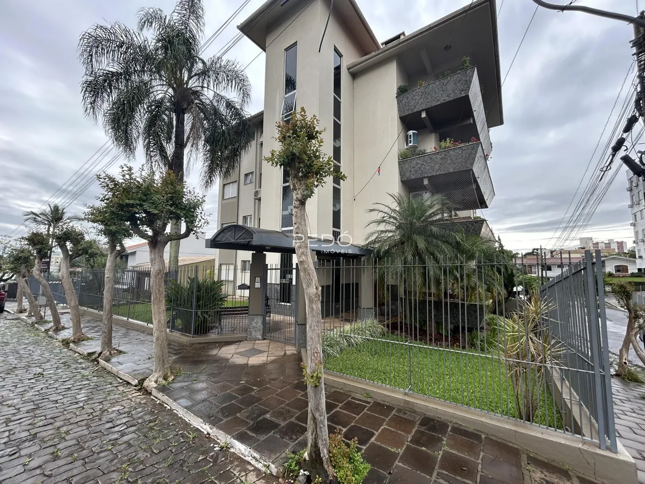 Fachada de um prédio residencial em Lajeado, Brasil, com árvores e cerca.