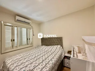 Quarto com cama grande e janela com persianas brancas.