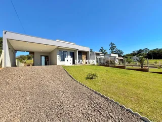 Fachada de uma casa moderna com jardim gramado e acesso por estrada de cascalho.