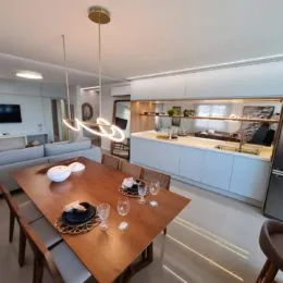 Ambiente de jantar com mesa de madeira e cozinha moderna em um imóvel.