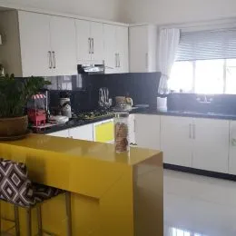 Cozinha moderna com armários brancos e ilha amarela em ambiente claro.