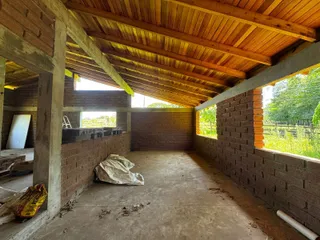 Vista interna de uma estrutura em construção com paredes de tijolo aparente e forro de madeira exposto.
