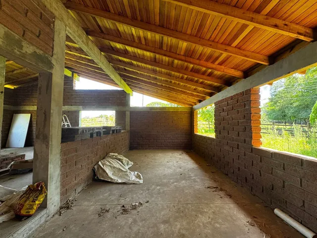 Vista interna de uma estrutura em construção com paredes de tijolo aparente e forro de madeira exposto.