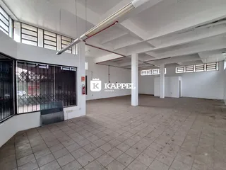 Vista interna de um espaço amplo com piso de cerâmica e estrutura de teto exposta.