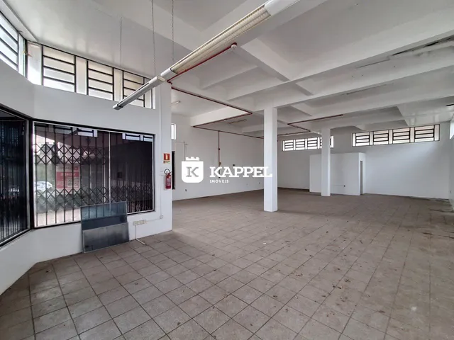 Vista interna de um espaço amplo com piso de cerâmica e estrutura de teto exposta.