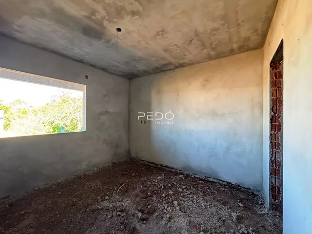 Interior de um cômodo com paredes de concreto aparente e piso de terra.