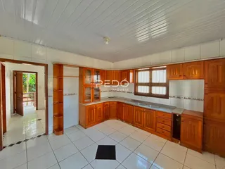 Vista interna de uma cozinha com armários de madeira e piso cerâmico claro.