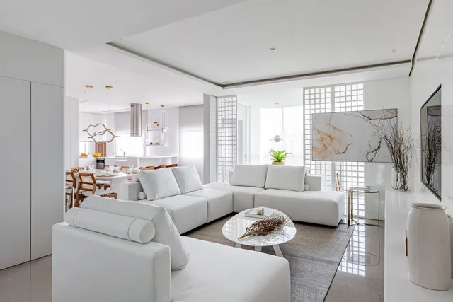 Sala de estar moderna com sofá branco e decoração clara em um apartamento.
