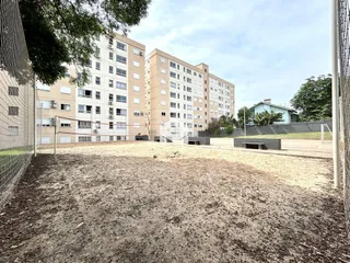 Vista externa de um terreno com grama e cerca em frente a um prédio residencial.