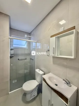 Foto de um banheiro com box de vidro e louças brancas.