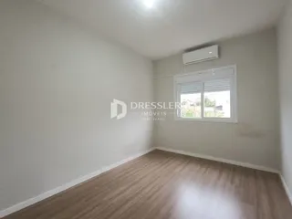Ambiente interno de uma sala com piso de madeira clara e paredes brancas.