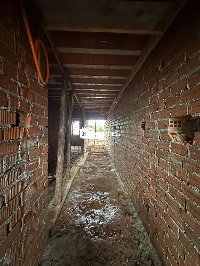 Vista de um corredor interno com paredes de tijolos aparentes e piso de terra.