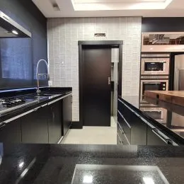 Vista interna de uma cozinha com armários escuros e revestimento de parede branco.