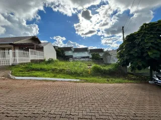 Vista externa de uma propriedade com pavimento de tijolos e vegetação no jardim.