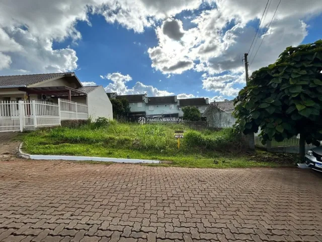 Vista externa de uma propriedade com pavimento de tijolos e vegetação no jardim.