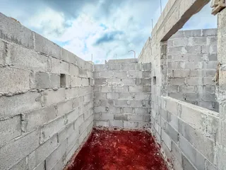 Parede de concreto cru de um espaço interno com piso de terra vermelha.