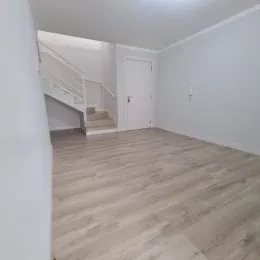 Interior de um ambiente com piso de madeira clara e escada visível.