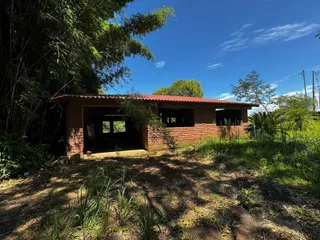 Fachada de um prédio de tijolos com telhado vermelho em uma área com vegetação alta.