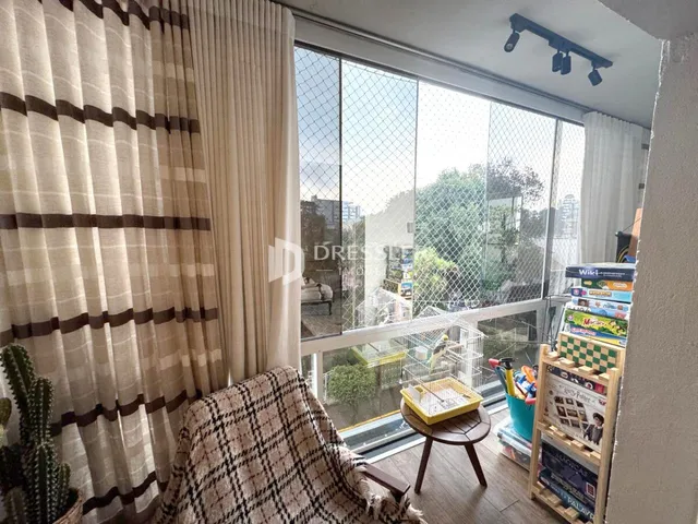 Vista da sala com cortinas claras e grandes janelas.