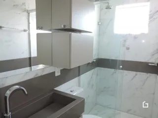 Banheiro com revestimento de mármore e box de vidro.