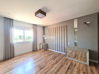 Sala de estar com piso de madeira clara e grandes janelas.